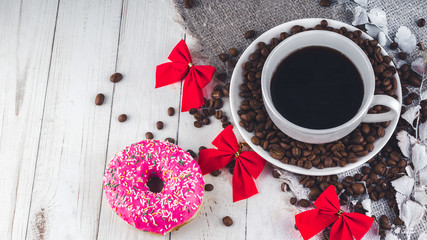 A hot cup of coffee with a doughnut and the coffee beans on the table. Composition of a delicious coffee and sweet snack.