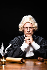 serious judge in judicial robe and wig looking at camera isolated on black