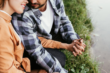 cropped view of man holding hand of girlfriend while spending time near lake