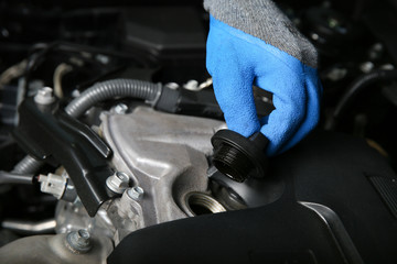 mechanic's hands in gloves are opening the oil filler cap in the car engine