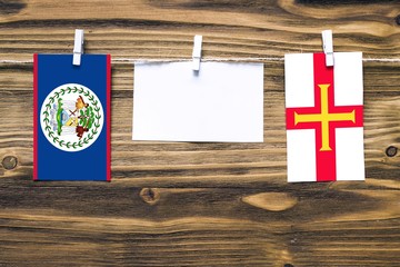 Hanging flags of Belize and Guernsey attached to rope with clothes pins with copy space on white...