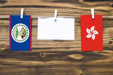 Hanging flags of Belize and Hong Kong attached to rope with clothes pins with copy space on white note paper on wooden background.Diplomatic relations between countries.