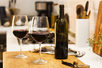 Copas con vino tinto y botella sobre tabla de madera rústica en la cocina. Vista de frente y de...