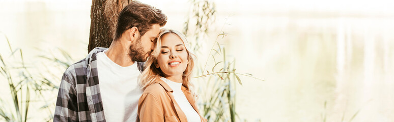panoramic shot of happy couple standing near lake in park