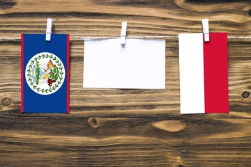 Hanging flags of Belize and Indonesia attached to rope with clothes pins with copy space on white...