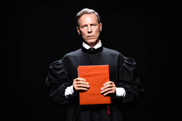 judge in judicial robe holding orange book isolated on black