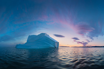 Early morning summer alpenglow lighting up icebergs during midnight season. Ilulissat, Greenland. Summer Midnight Sun and icebergs. Blue ice in icefjord. Affected by climate change and global warming.