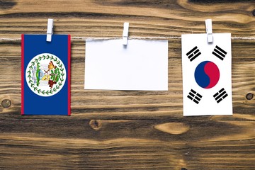 Hanging flags of Belize and South Korea attached to rope with clothes pins with copy space on white note paper on wooden background.Diplomatic relations between countries.