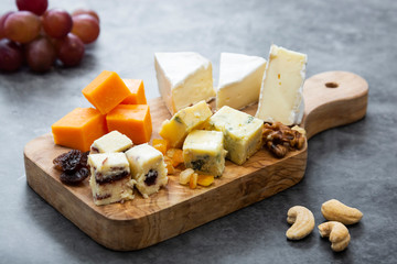 Various different types of cheese slices, cheese mix on wooden cutting board. Wine snack. Camembert, parmesan, brie cheese.