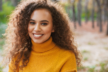 Happy optimistic young curly woman walking in park