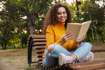 Beautiful curly woman sit in park outdoors reading book.