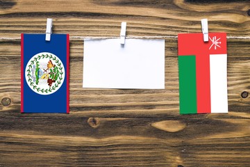 Hanging flags of Belize and Oman attached to rope with clothes pins with copy space on white note paper on wooden background.Diplomatic relations between countries.