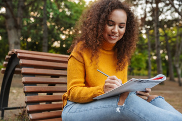 Woman sit on bench in park outdoors writing notes