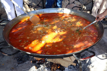 Paella is cooked in a large frying pan over an open fire.