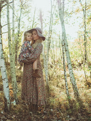 beautiful young mother walks with her daughter in the forest. beautiful sunset light, boho style girl, girl in a hat, happy motherhood.