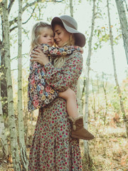 beautiful young mother walks with her daughter in the forest. beautiful sunset light, boho style girl, girl in a hat, happy motherhood.