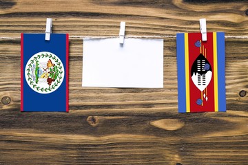 Hanging flags of Belize and Swaziland attached to rope with clothes pins with copy space on white...