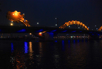 Yellow illuminated Dragon Bridge in Da Nang at night reflected in Han river, Vietnam 