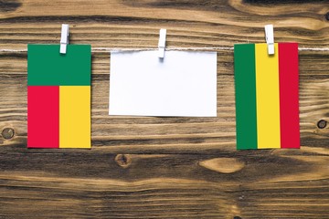 Hanging flags of Benin and Bolivia attached to rope with clothes pins with copy space on white note paper on wooden background.Diplomatic relations between countries.