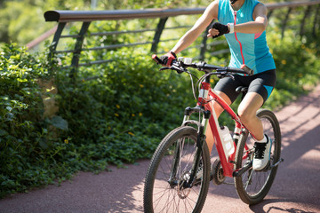 Fototapeta premium Woman cyclist looking at her smartwatch while riding bike on sunny day
