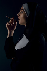Profile shot of upper nun's body, posing on black background. She wearing dark nun's clothing. The...