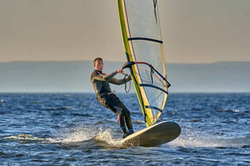 A male athlete is interested in windsurfing. He moves on a Sailboard on a large lake on an autumn...