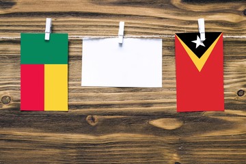 Hanging flags of Benin and East Timor attached to rope with clothes pins with copy space on white...