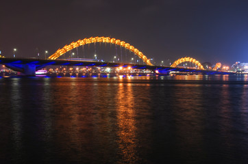Obraz na płótnie Canvas Yellow illuminated Dragon Bridge in Da Nang at night reflected in Han river, Vietnam 