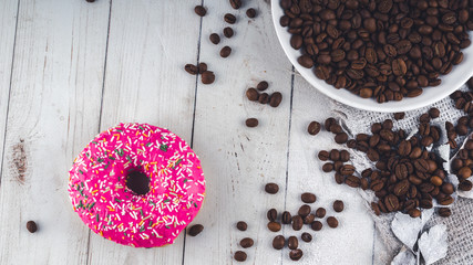 A delicious donut near a small white plate with coffee beans. The coffee beans are scattered on the table for decoration. Close up.
