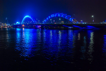 Blue illuminated Dragon Bridge in Da Nang at night reflected in Han river, Vietnam 