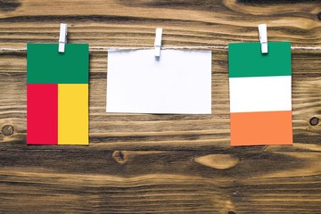 Hanging flags of Benin and Ireland attached to rope with clothes pins with copy space on white note paper on wooden background.Diplomatic relations between countries.