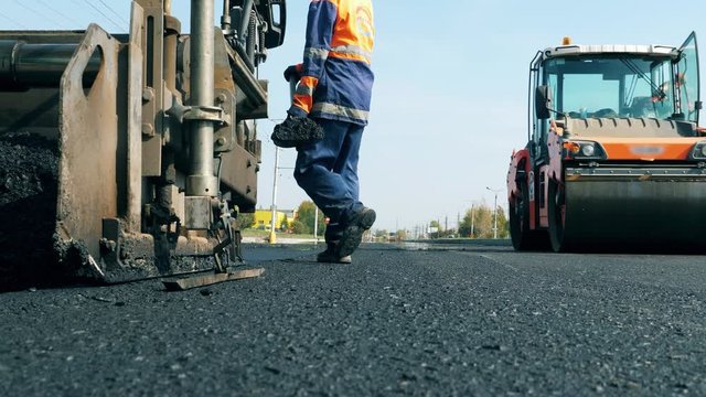 Man works on a road with machines, laying asphalt.