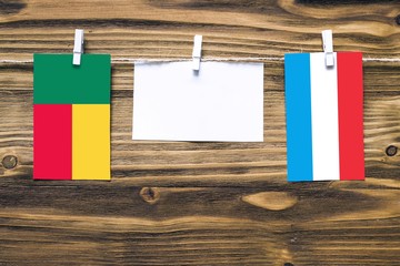 Hanging flags of Benin and Luxembourg attached to rope with clothes pins with copy space on white note paper on wooden background.Diplomatic relations between countries.