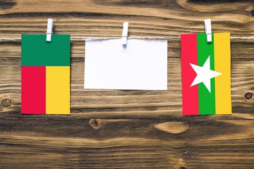 Hanging flags of Benin and Myanmar attached to rope with clothes pins with copy space on white note...