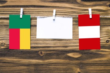 Hanging flags of Benin and Peru attached to rope with clothes pins with copy space on white note paper on wooden background.Diplomatic relations between countries.