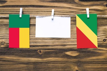 Hanging flags of Benin and Republic Of The Congo attached to rope with clothes pins with copy space on white note paper on wooden background.Diplomatic relations between countries.