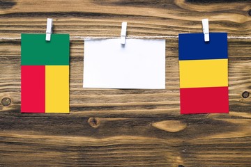 Hanging flags of Benin and Romania attached to rope with clothes pins with copy space on white note paper on wooden background.Diplomatic relations between countries.