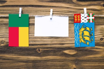 Hanging flags of Benin and Saint Pierre And Miquelon attached to rope with clothes pins with copy space on white note paper on wooden background.Diplomatic relations between countries.