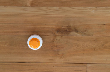 Closeup of white smoke detector with orange cover on the wooden ceiling of the building.