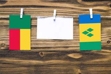 Hanging flags of Benin and Saint Vincent And The Grenadines attached to rope with clothes pins with copy space on white note paper on wooden background.Diplomatic relations between countries.