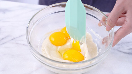 Mixing egg yolk into cake batter with green rubber spatula mixer tool stirring until smooth and...