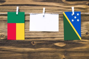 Hanging flags of Benin and Solomon Islands attached to rope with clothes pins with copy space on...