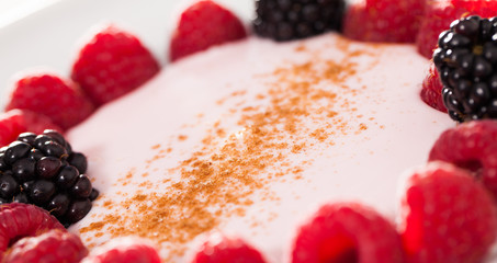 raspberries and blackberries laid out on a white plate in circle with yogurt and cinnamon