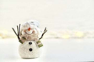 Single white cheerful snowman smiling and standing on a background with snow and lights
