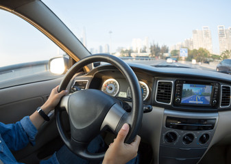 People hands holding steering wheel while driving car on city road