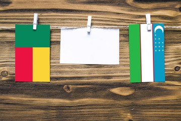 Hanging flags of Benin and Uzbekistan attached to rope with clothes pins with copy space on white note paper on wooden background.Diplomatic relations between countries.