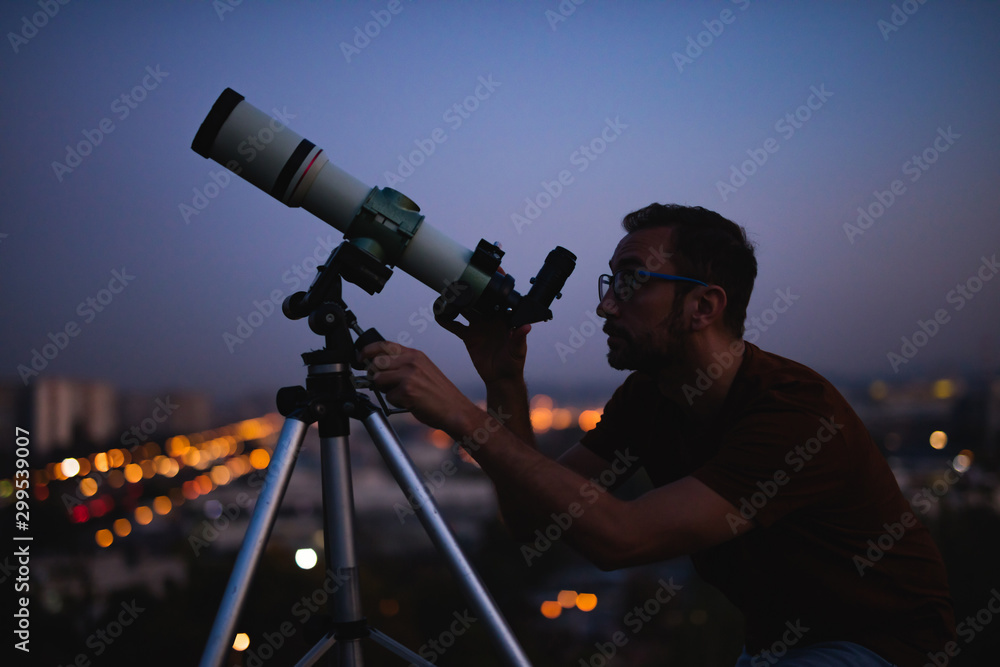 Canvas Prints astronomer with a telescope watching at the stars and moon with blurred city lights in the backgroun
