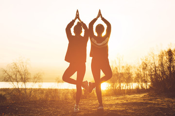 Silhouette of two girls doing yoga at sunset in nature