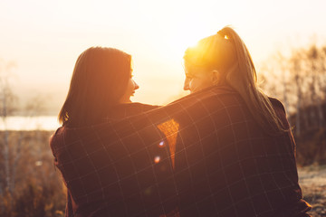 Two girlfriends are sitting under a blanket and laughing. Female friendship and outdoor recreation.