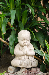 Cute little Buddha stone statue praying and smiling with eyes closed